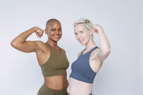 Free Cheerful diverse fit females in sportswear pumping biceps muscle and looking at camera while standing against white background Stock Photo