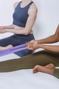 Crop person stretching resistance band sitting on floor with partner