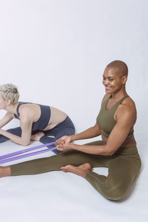 Diverse athletes in sportswear practicing fitness exercise with resistance bands during workout in light studio