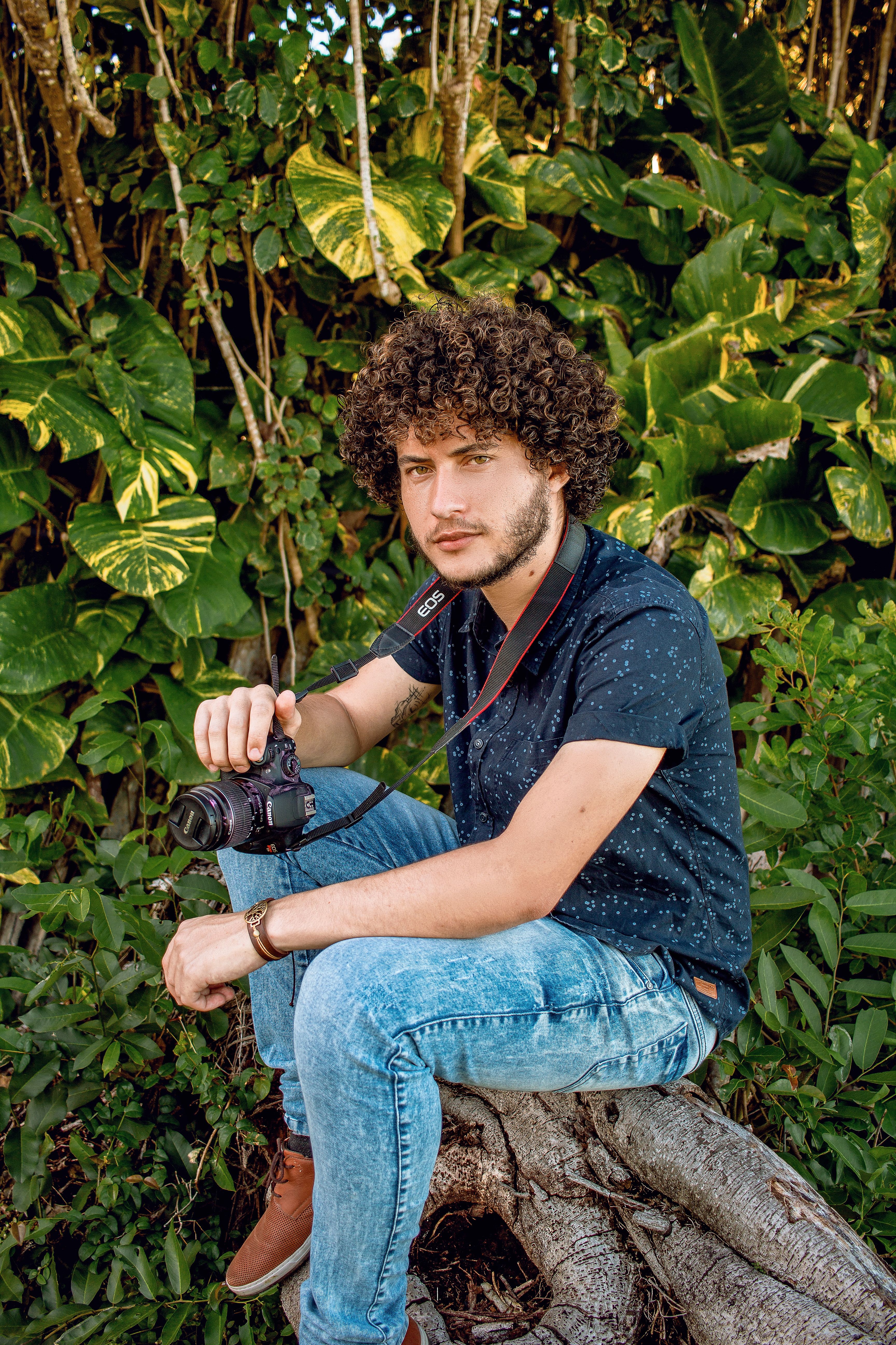 Young male photographer with curly hair sitting outdoors with a camera.