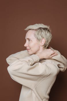 Side profile of a woman with short hair wearing a beige hoodie against a brown background.