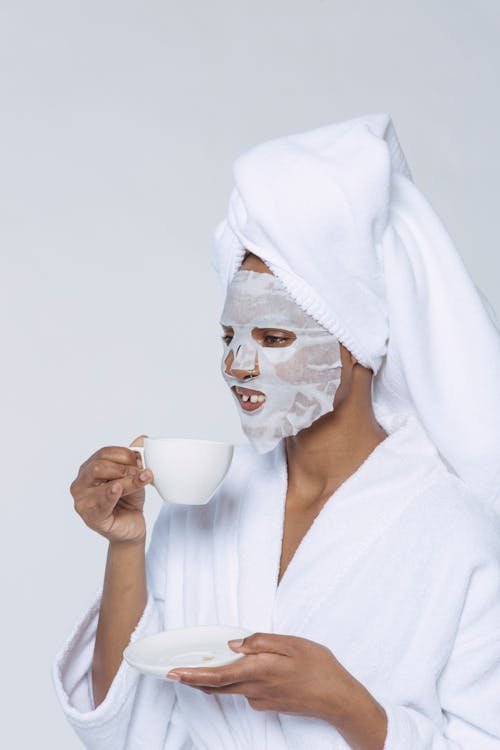 Black woman in sheet mask drinking coffee in morning
