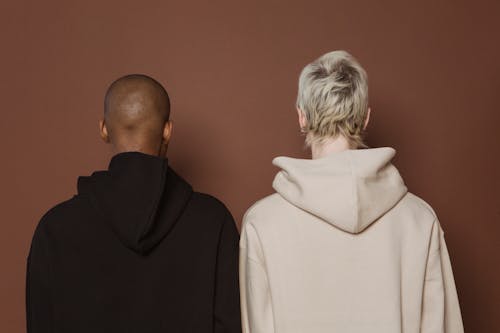 Back view of unrecognizable multiethnic female models wearing comfy hoodies standing against brown background