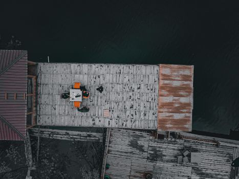Drone shot of a wooden dock beside a lake, featuring people sitting around a table with visible shed structures.