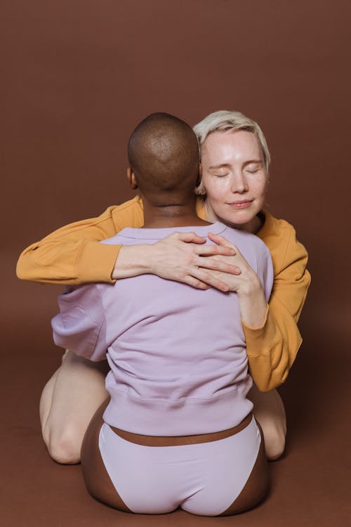 Free Enamored multiethnic lesbian couple hugging in brown studio Stock Photo