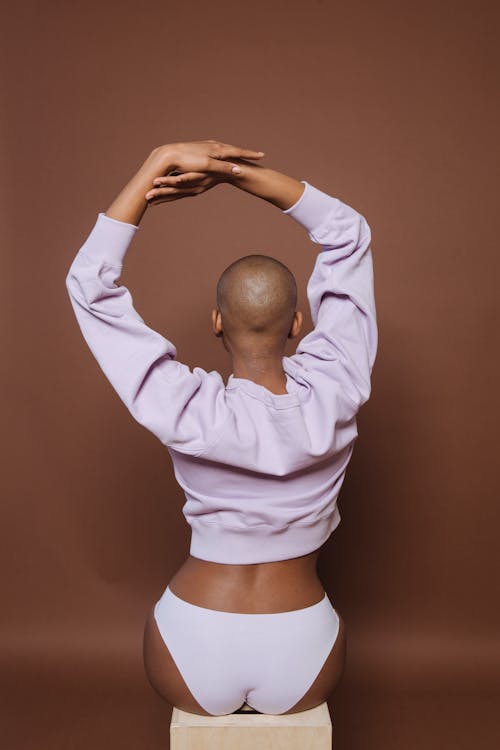 Free Anonymous bald black female model with raised hands in brown studio Stock Photo