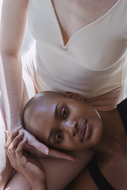 Free From above of calm African American female with bald head lying on anonymous female and looking at camera in sunlight Stock Photo