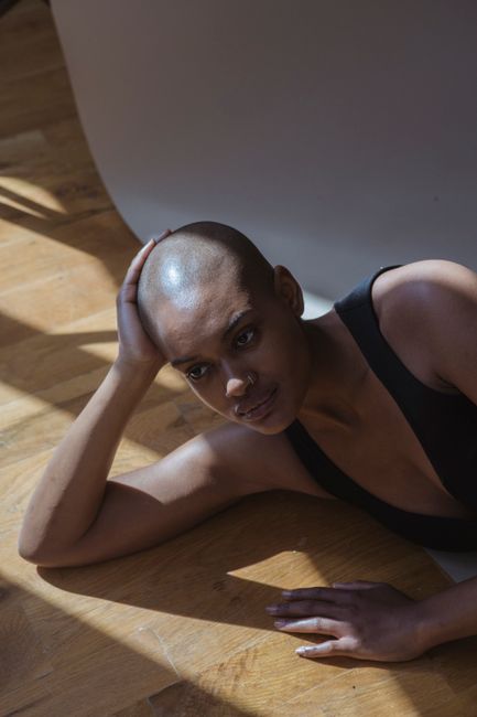 African American woman touching head while looking forward and lying on floor with shadows in photo studio
