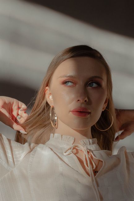 Young contemplative female in blouse and earrings looking away in sunbeam on blurred background