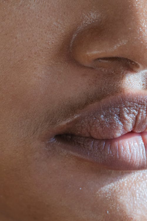 Closeup of crop anonymous ethnic person with sensitive lips and blackheads on oily skin with shadow