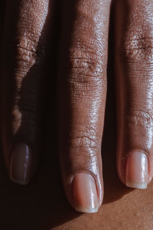 Hand with long fingers with nails of crop anonymous African American female in light room with bright sunlight and shadow