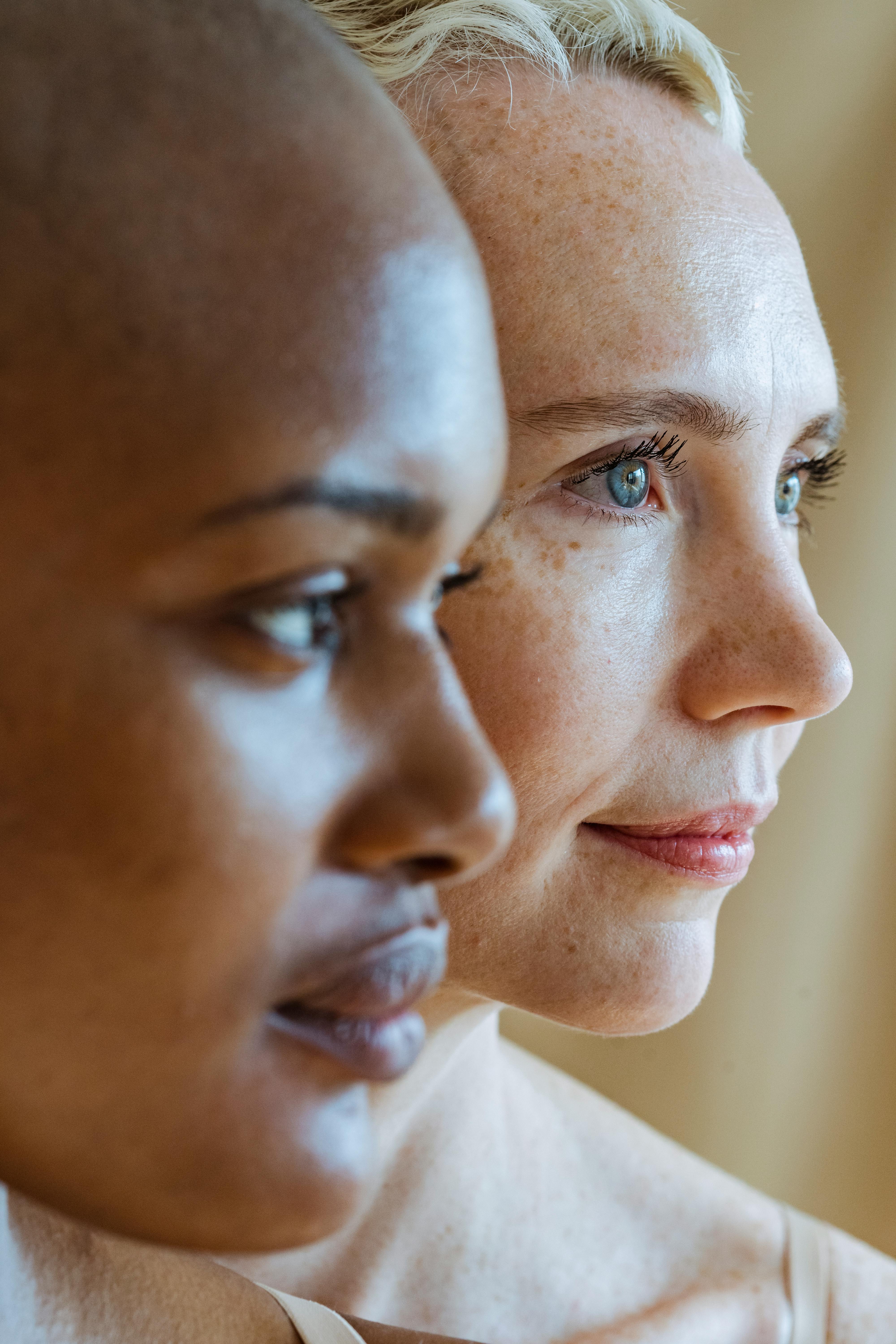 Two diverse women gaze thoughtfully, with soft light highlighting their profiles.