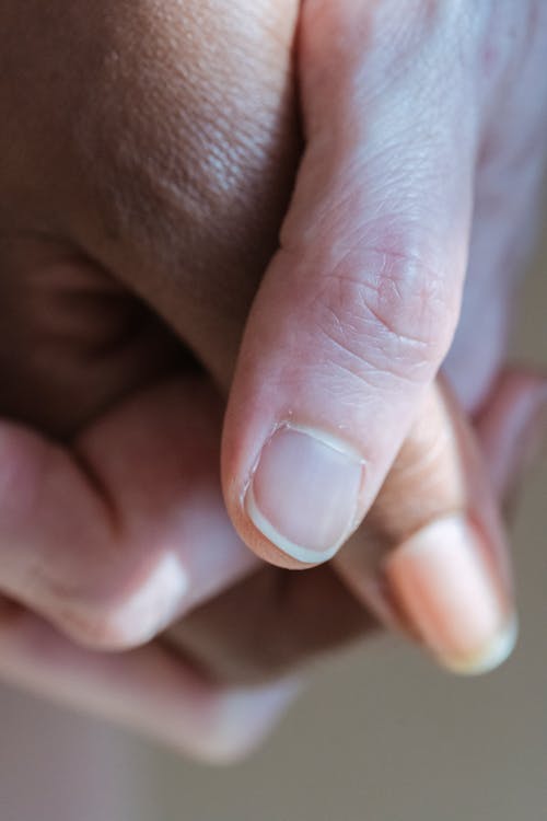 Closeup of crop unrecognizable multiracial couple holding hands against light blurred background in sunny day