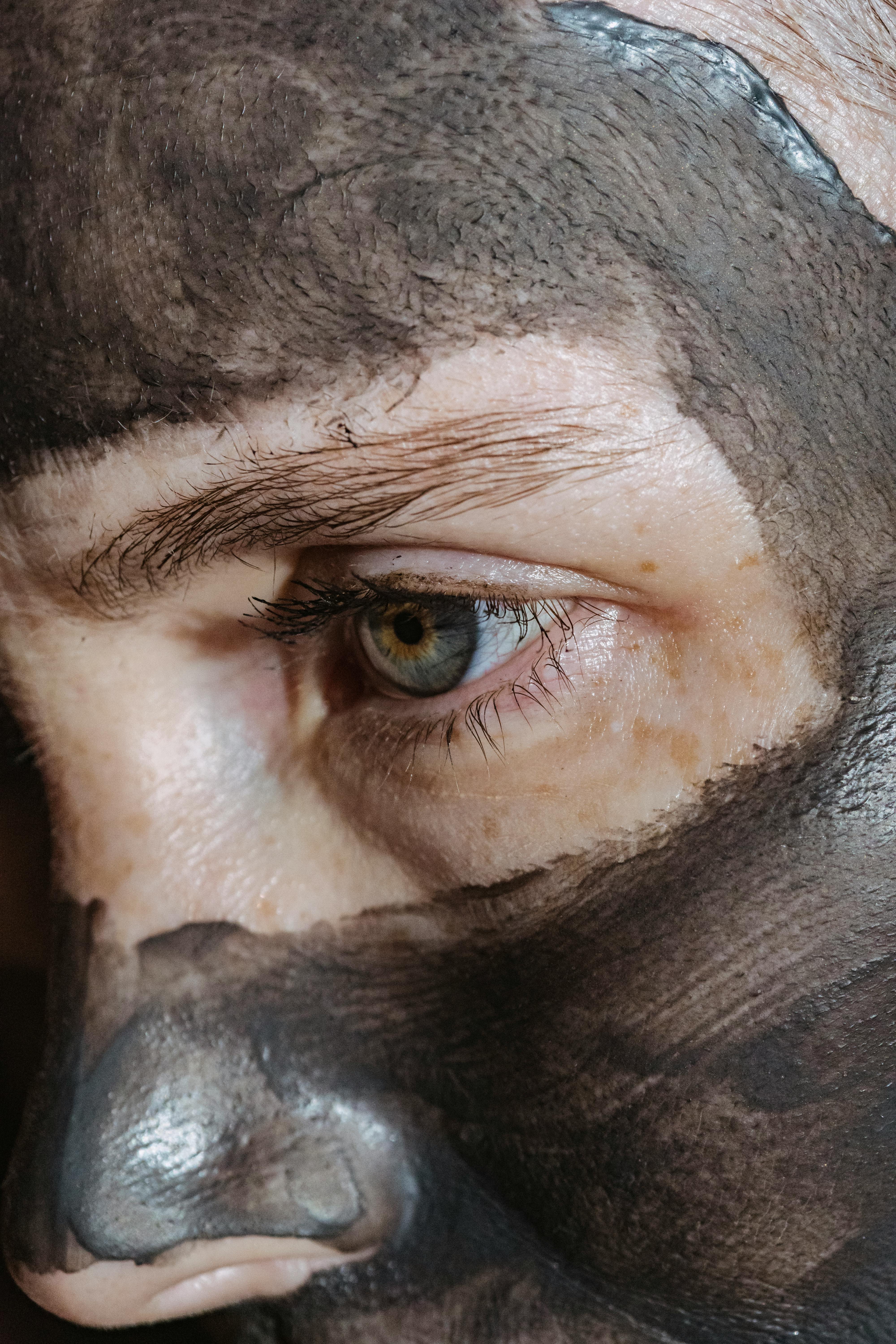 Closeup of crop pensive female with blue eyes and anti aging clay mask on face looking away in daylight