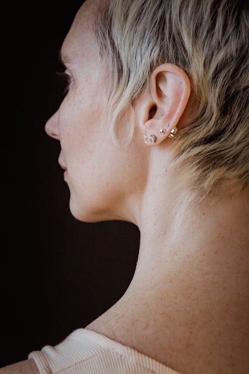 Free Back view of crop female with short hair and shiny earrings looking away on black background Stock Photo