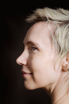 Side view portrait of young gorgeous female with short hair and earrings smiling and looking away on black background