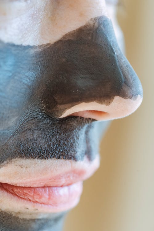 Free Crop unrecognizable female with black clay mask applied on face on blurred background in light room Stock Photo
