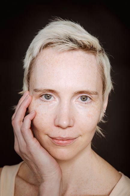 Beautiful young female with short blond hair smiling and touching face while looking at camera on black background