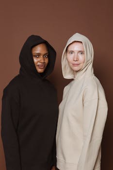 Multiracial female models in black and white hoodies standing against brown background in studio and looking at camera