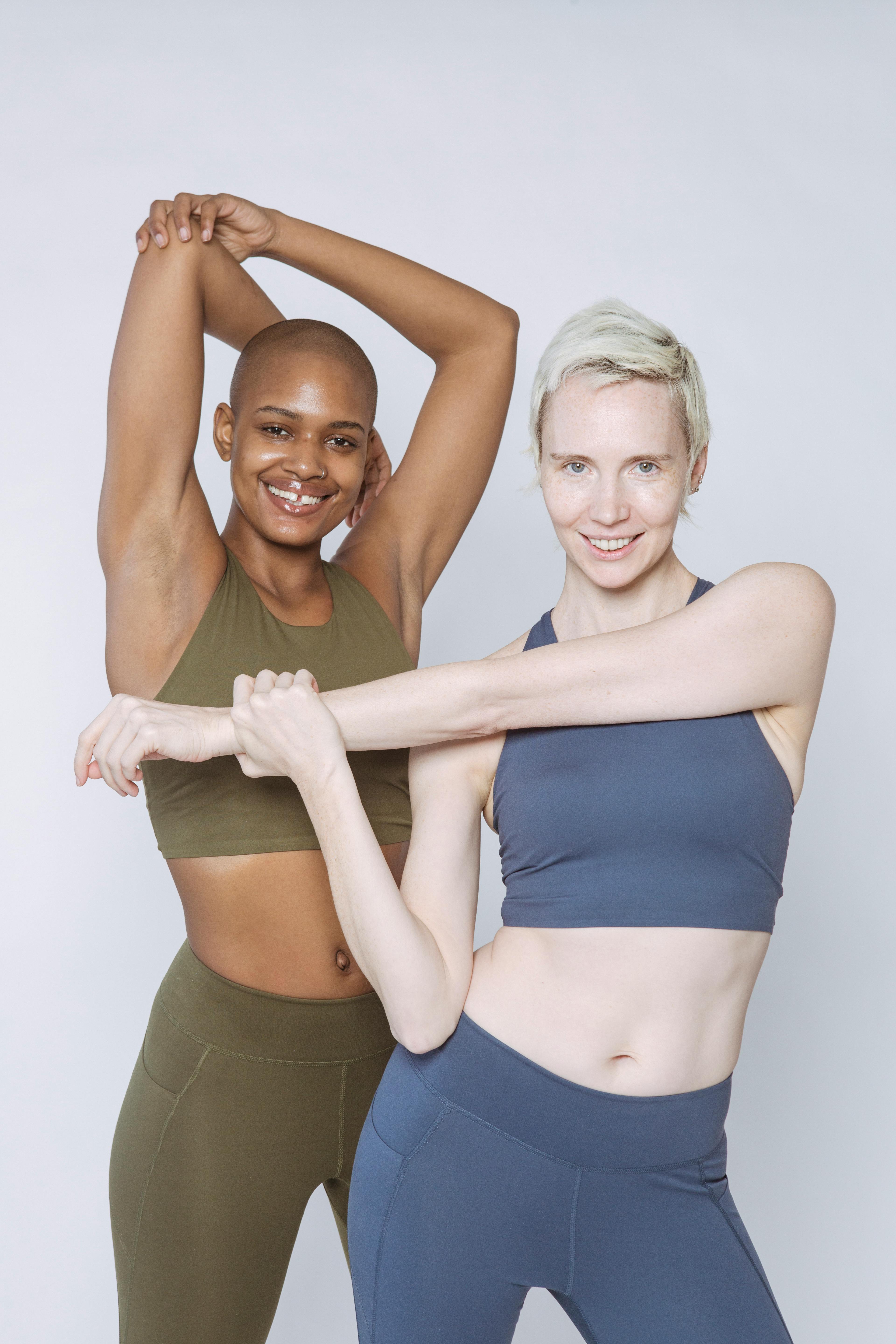 cheerful multiracial women in activewear stretching arms in studio