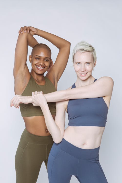 Free Diverse female models in sportswear smiling and looking at camera while stretching arms against white background Stock Photo