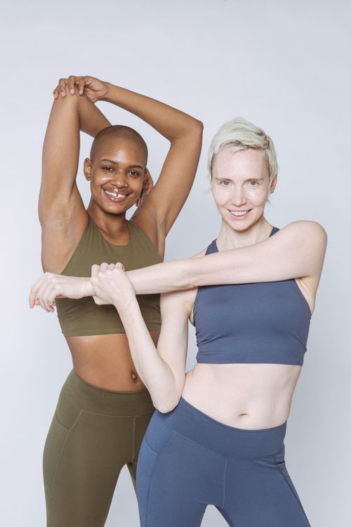 Free Diverse female models in sportswear smiling and looking at camera while stretching arms against white background Stock Photo