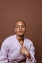 African American model with shaved head looking away while touching pink long sleeve shirt on brown background