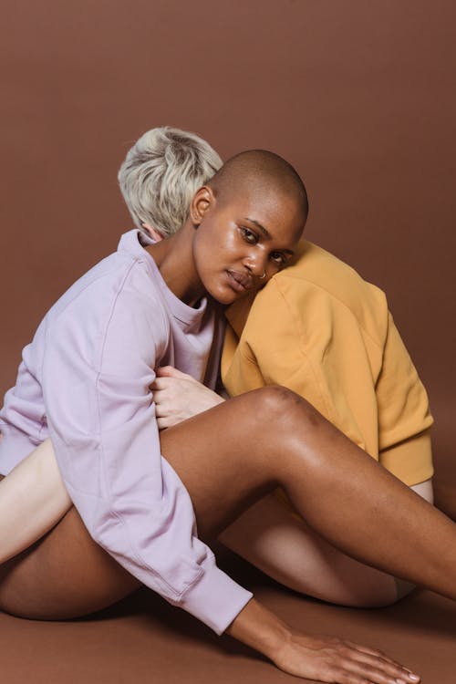 Free Side view of diverse models sitting on floor and putting heads on shoulders of each other against brown background Stock Photo