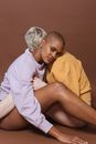 Side view of diverse models sitting on floor and putting heads on shoulders of each other against brown background