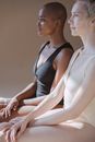 Side view of multiracial females with short hair in contrast bodysuits sitting and looking away while meditating in light studio