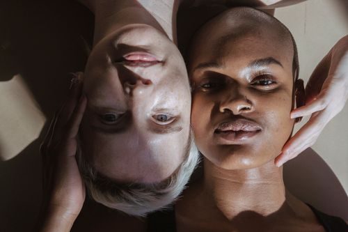 Free Top view of emotionless multiracial female models lying on floor touching face and looking at camera in daylight Stock Photo