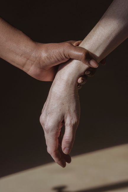 Crop anonymous couple in light studio while person grabbing and holding wrist of friend in beam of sunlight
