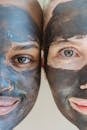 Crop cheerful multiethnic ladies with clay mask applied on faces looking at camera