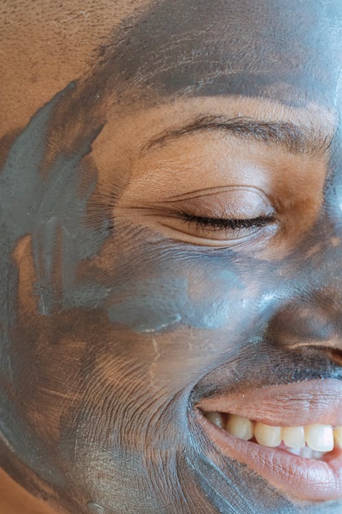 Crop black cheerful woman with clay mask and closed eyes