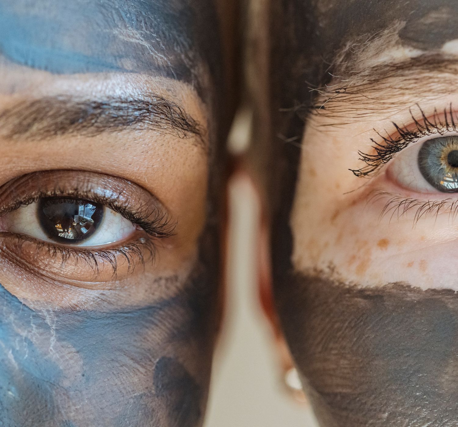 Closeup of diverse crop females with clay mask on faces looking at camera during skincare