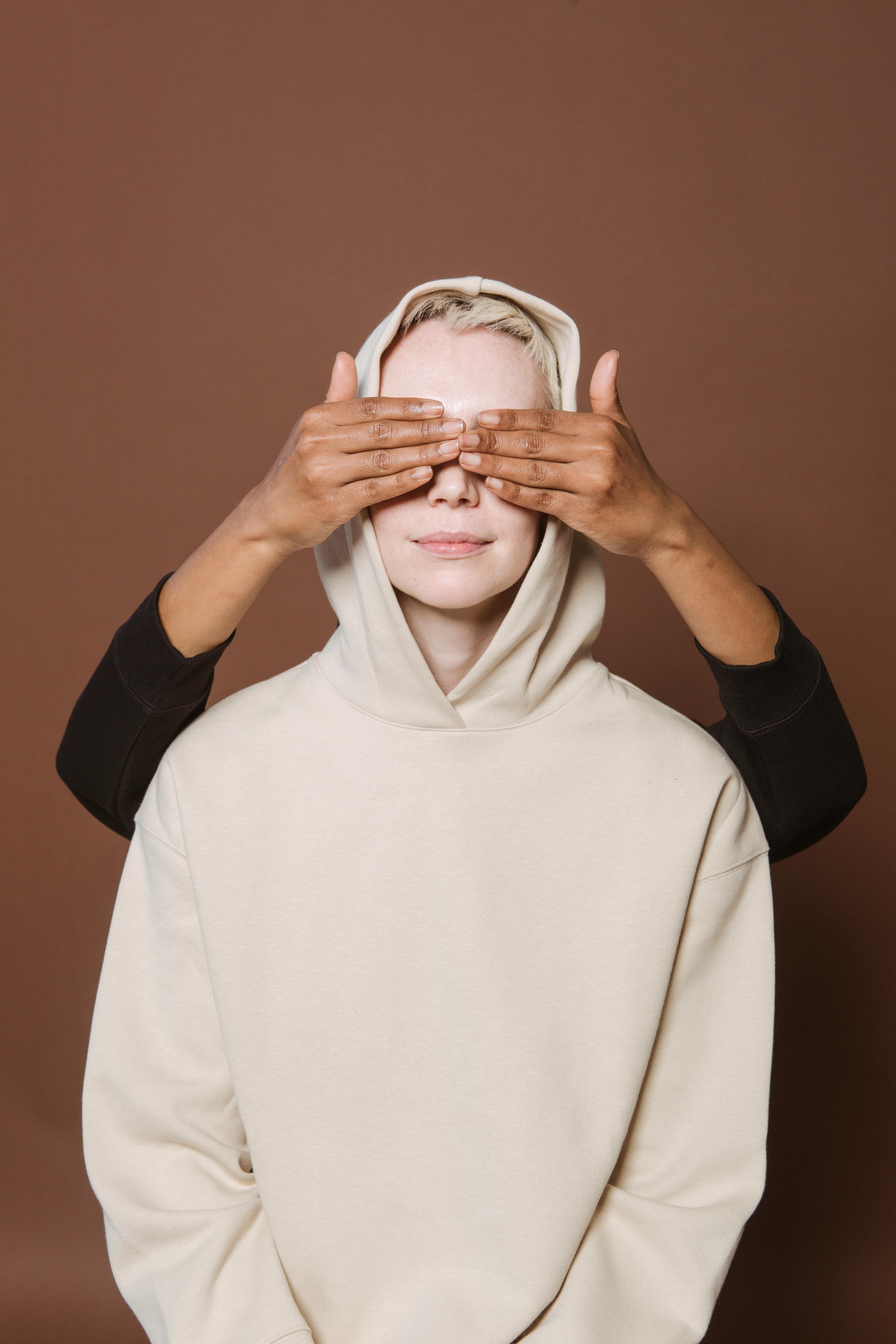 anonymous black woman covering eyes of female friend in brown studio