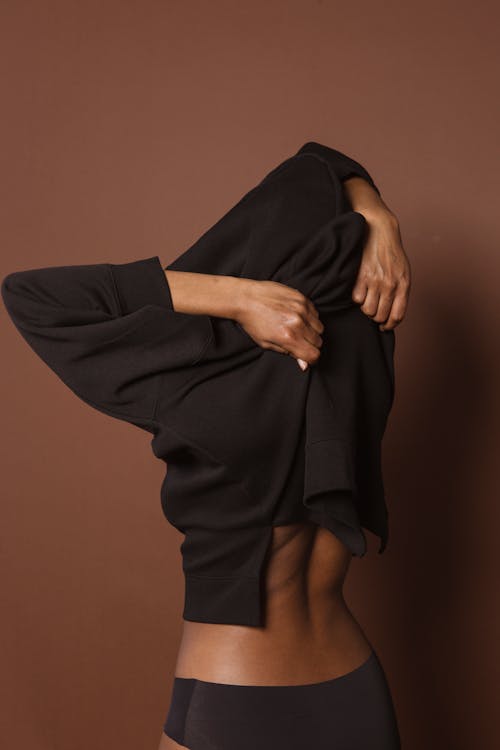 Free Anonymous fit black woman putting on sweatshirt in studio Stock Photo
