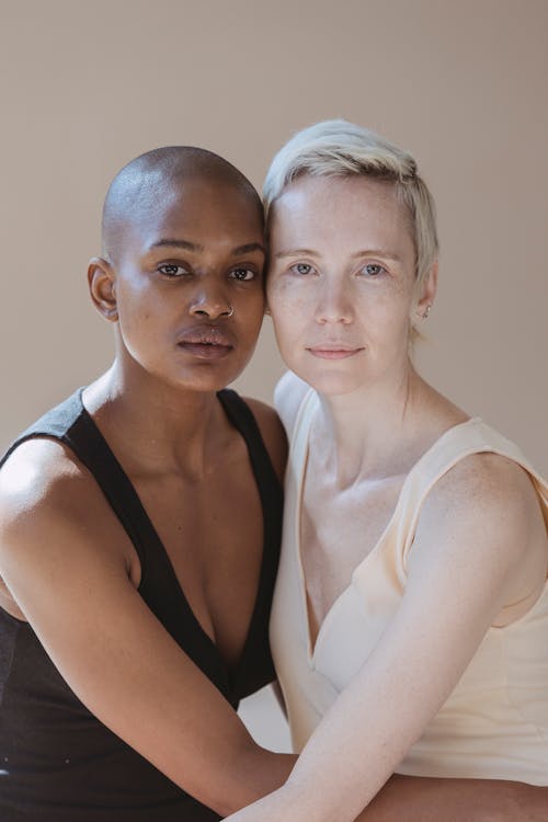 Free Calm diverse female models with natural makeup wearing casual clothes sitting close to each other and looking at camera Stock Photo