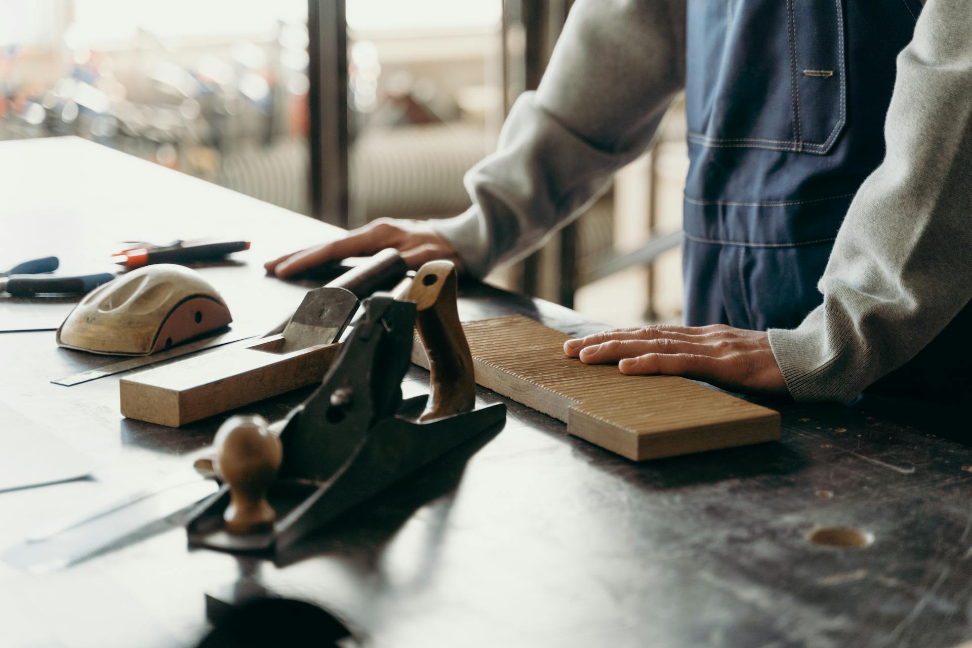 Carpenter working with tools and wood on a table in an industrial workshop.