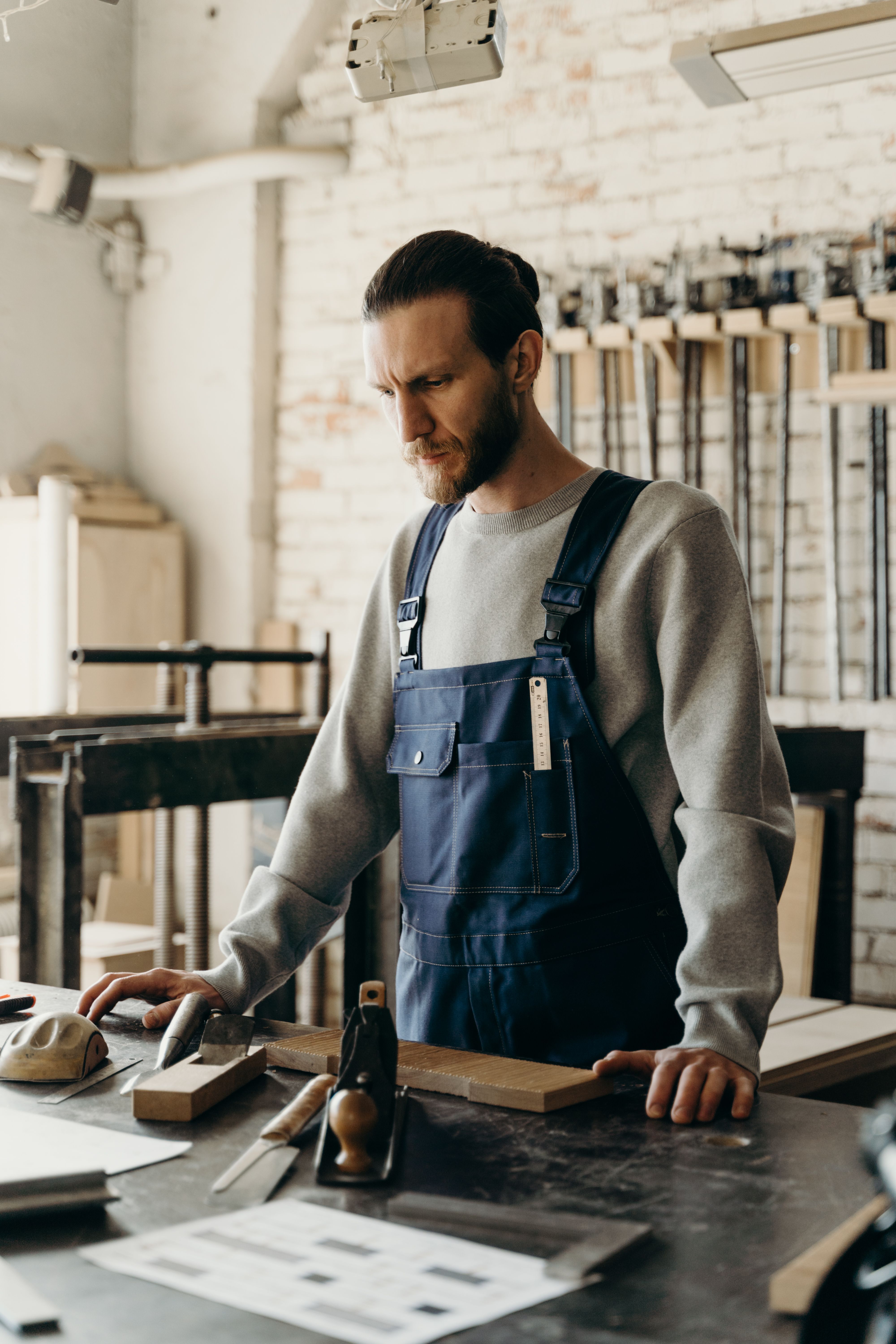 Craftsman in apron working with tools on a wooden workbench in a well-lit workshop.