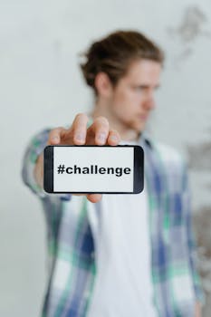 A young man in casual clothing holds a smartphone displaying '#challenge', focusing on motivation.