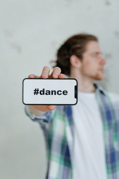 A blurred man holding a smartphone displaying a #dance hashtag, emphasizing dance culture and technology.