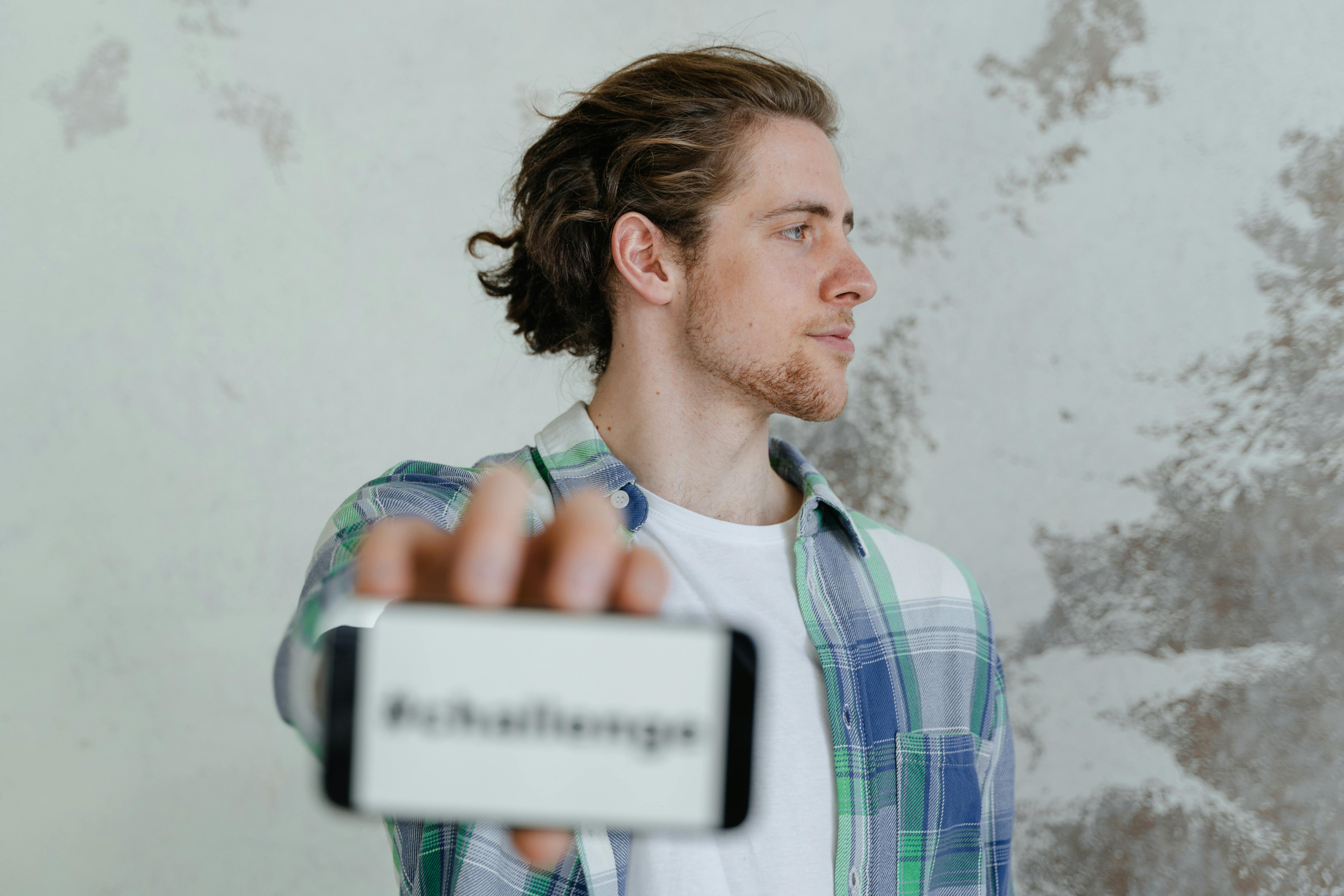 Profile of young man holding smartphone displaying text message in casual setting.