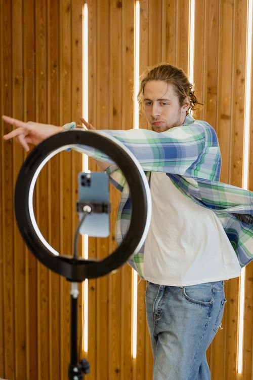 Free A stylish young man dances energetically in front of a smartphone and ring light setup, creating content. Stock Photo