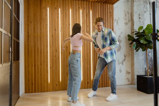 A young couple dances together in a modern indoor setting, having fun in casual outfits.
