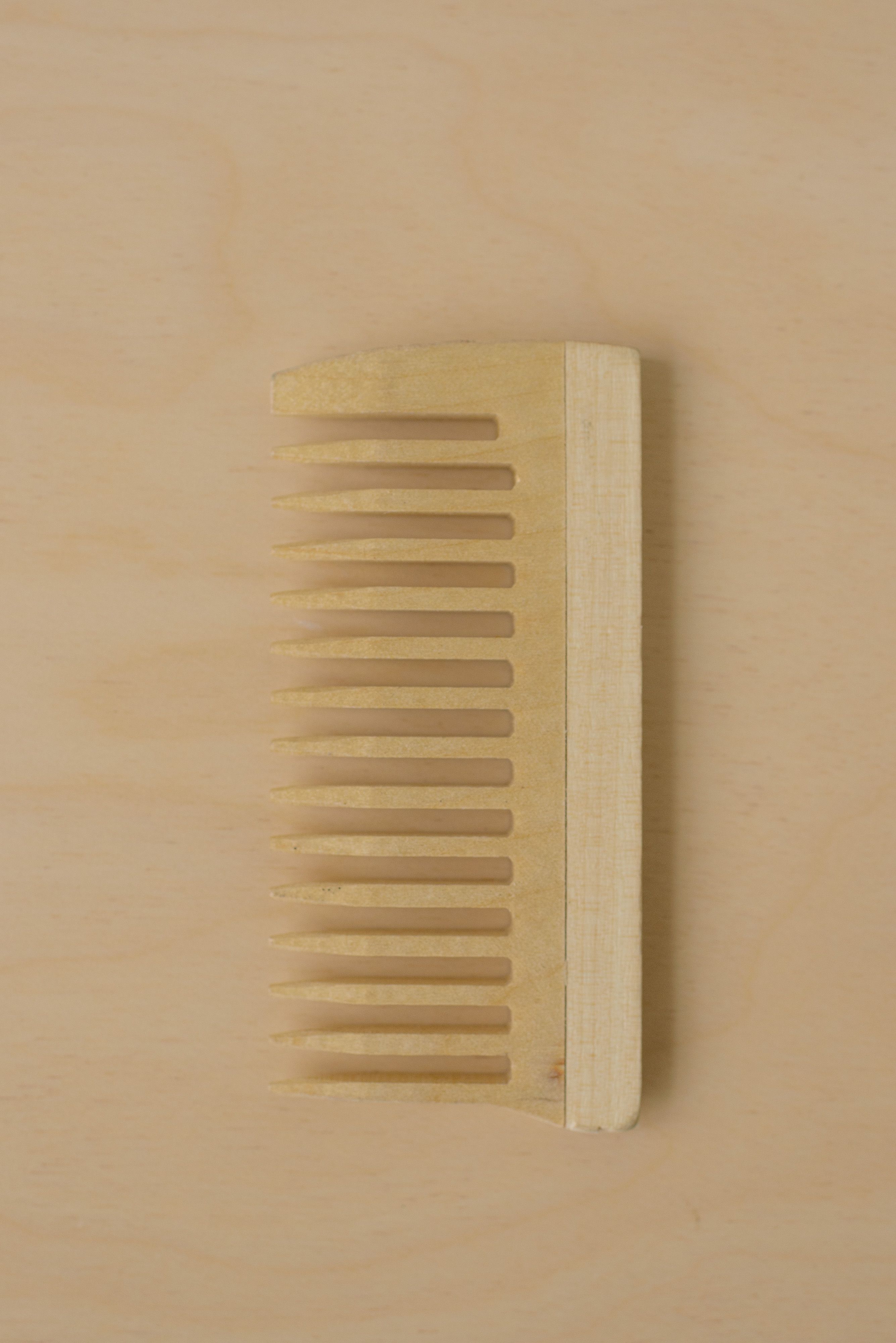 A wooden comb laid flat on a beige background, captured in a minimalist style.