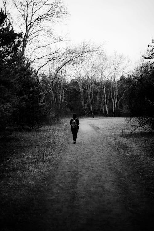 Grayscale Photo of a Person Walking on Dirt Road
