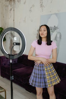 A young woman recording content with a ring light and phone indoors, showcasing modern lifestyle.