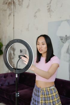 Teenage girl filming at home with a ring light and smartphone. Casual setting.