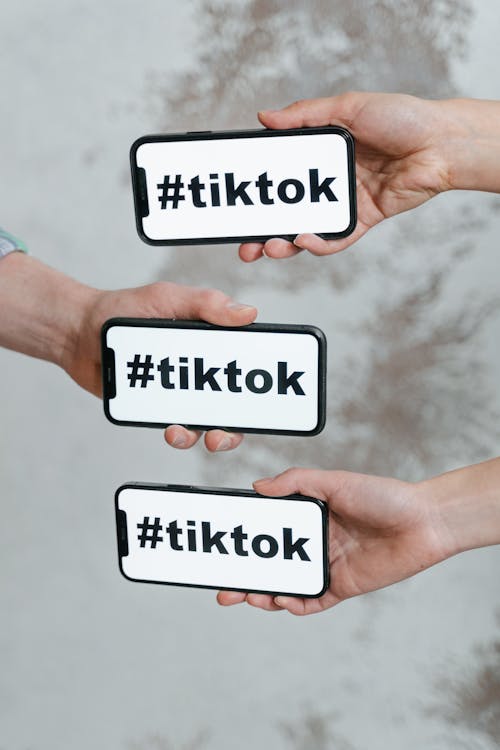 Free Hands holding smartphones displaying TikTok hashtag, emphasizing social media connection. Stock Photo
